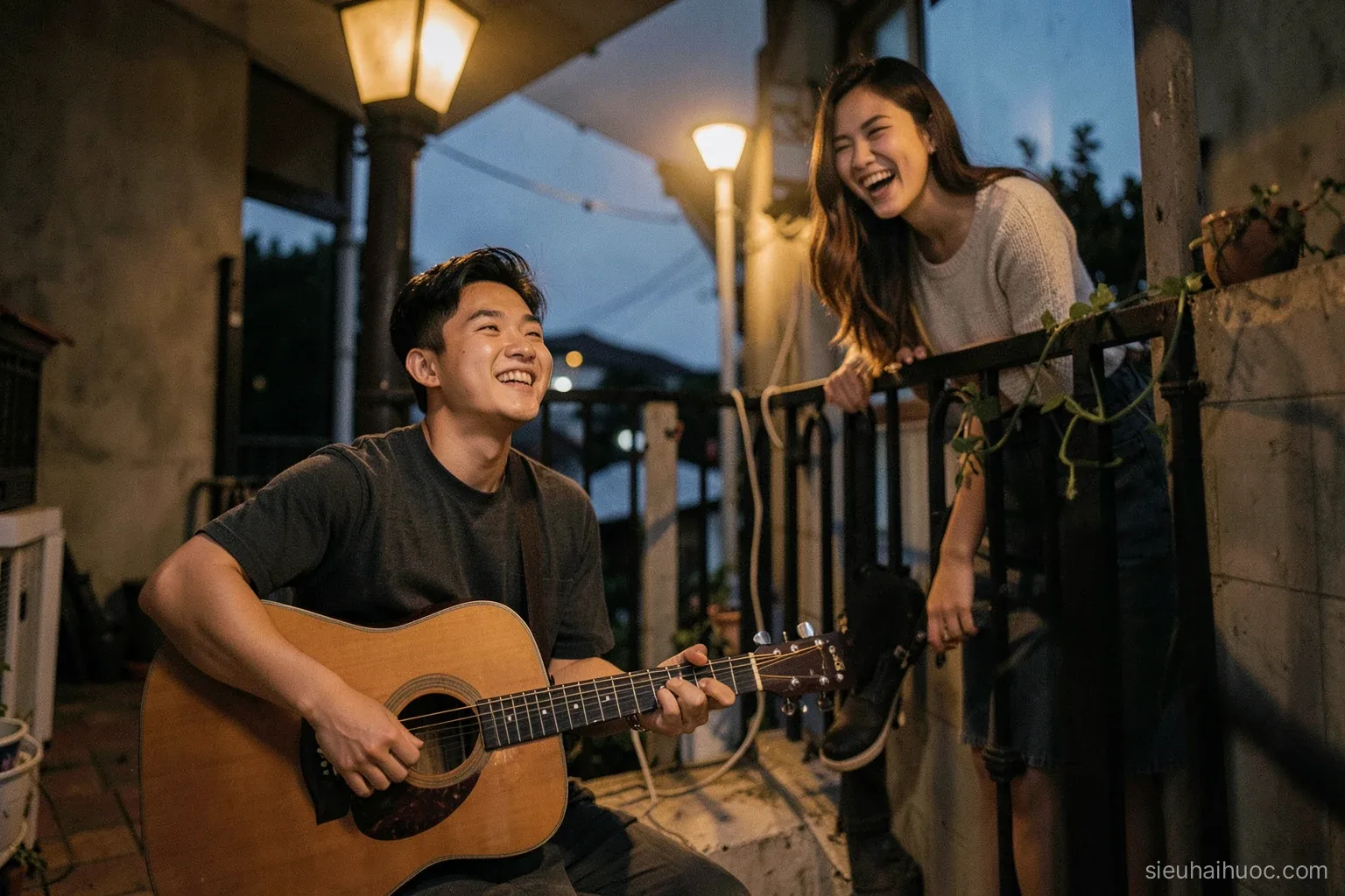 A young Vietnamese man holding an acoustic guitar under a balcony at dusk, a woman leaning on the railing above laughing, street light glowing, wide shot