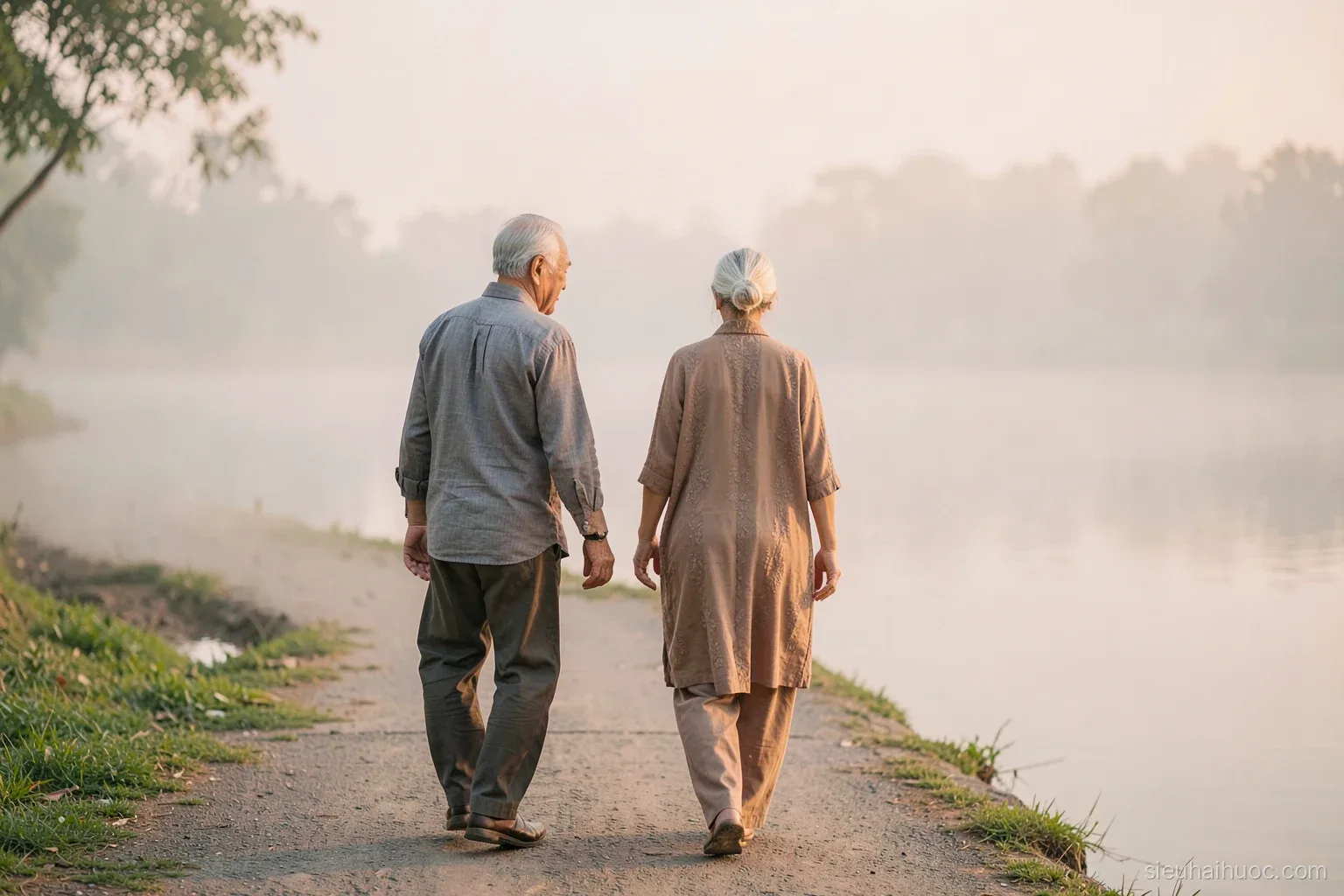 An elderly Vietnamese couple walking slowly along a lakeside path in the early morning mist, the man turning back to wait for the woman, soft pastel light
